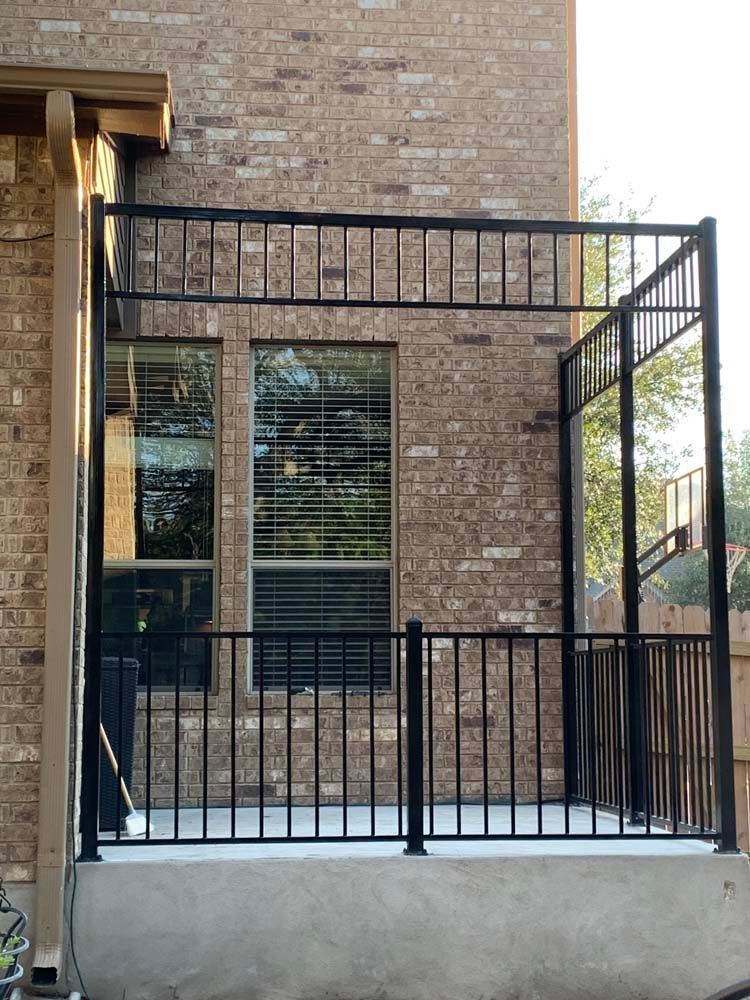 Black metal railing on a concrete patio next to a brick building.