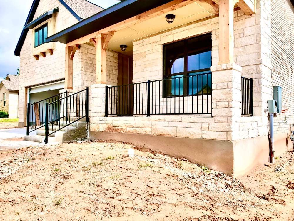 Exterior view of a house under construction with a porch and brick facade, a ramp leading to the garage.