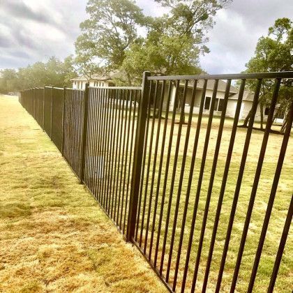 Black metal fence in a grassy yard, with a house and trees in the background under a cloudy sky.