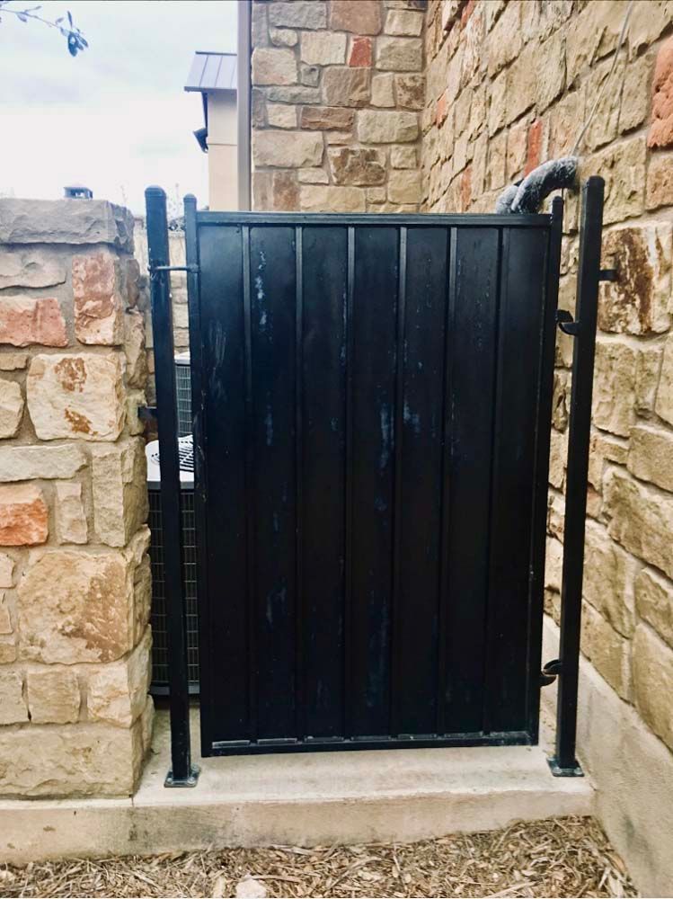 Black wooden gate between stone pillars, set in concrete, with black metal posts.
