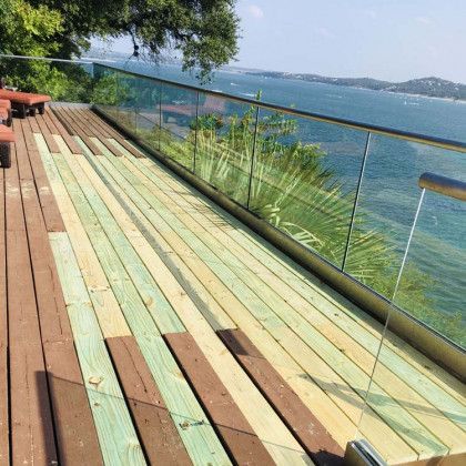 Wooden deck with glass railing overlooking water; some planks are new and green.