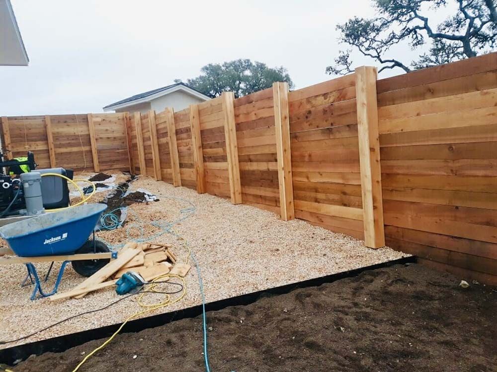 A wooden fence with gravel base in a yard with construction tools and equipment.
