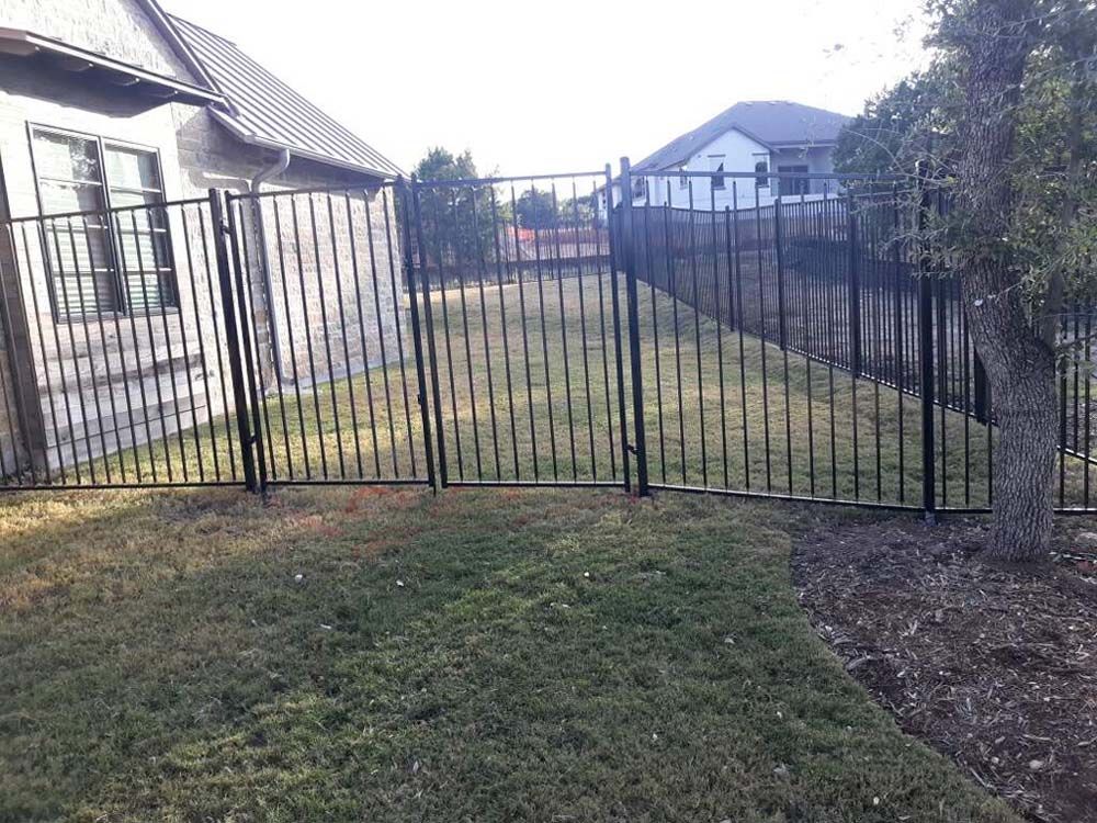 Black metal fence encloses a grassy backyard with a house, tree, and other houses in the distance.