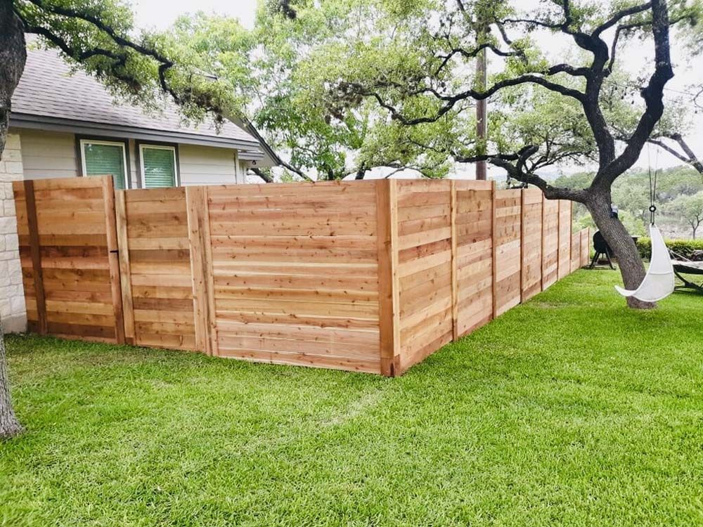 Wooden fence surrounding a grassy backyard with a house in the background. A swing hangs from a tree.