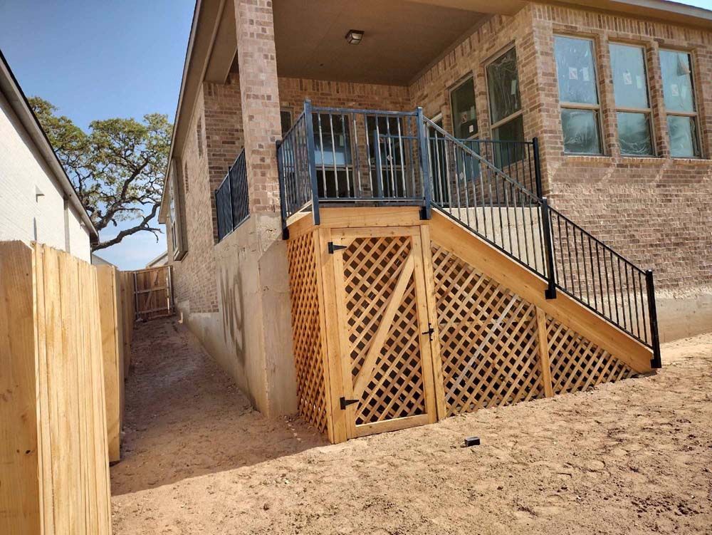 Wooden deck with lattice panels and black railing, built against a brick house on a sloped yard.