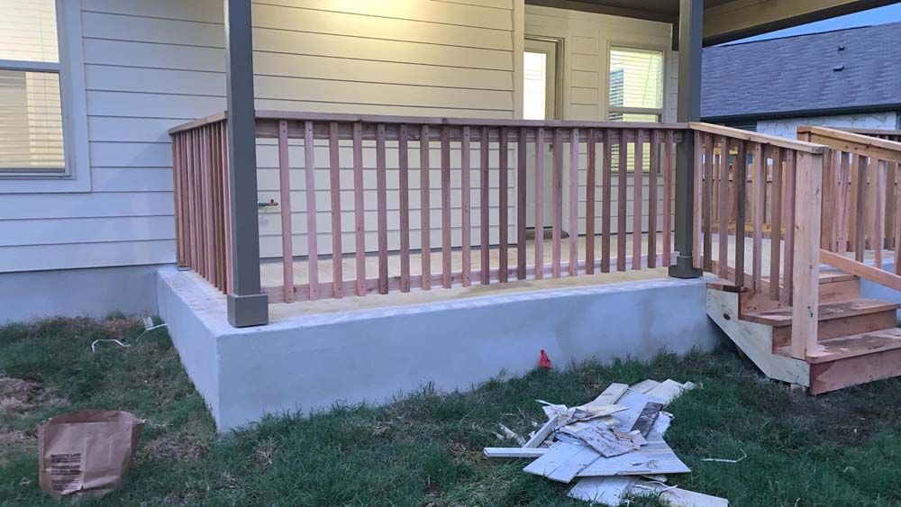 Unfinished wooden porch with railing and a ramp, surrounded by grass.