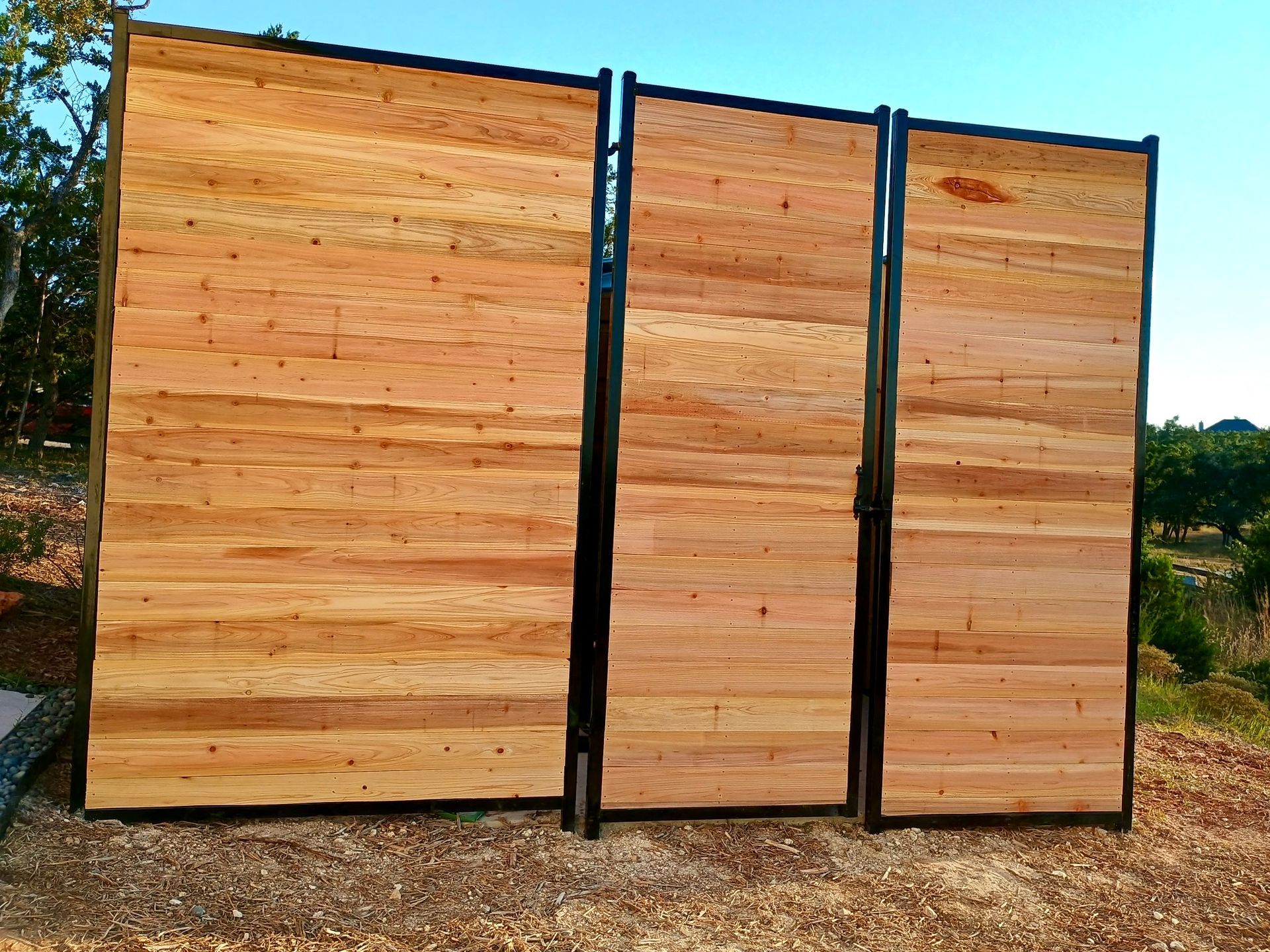 Three wooden panels in black metal frames, set outside on a gravel-covered ground.