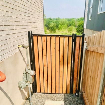 Wooden gate with black frame, between brick and wooden fences, leading to greenery.