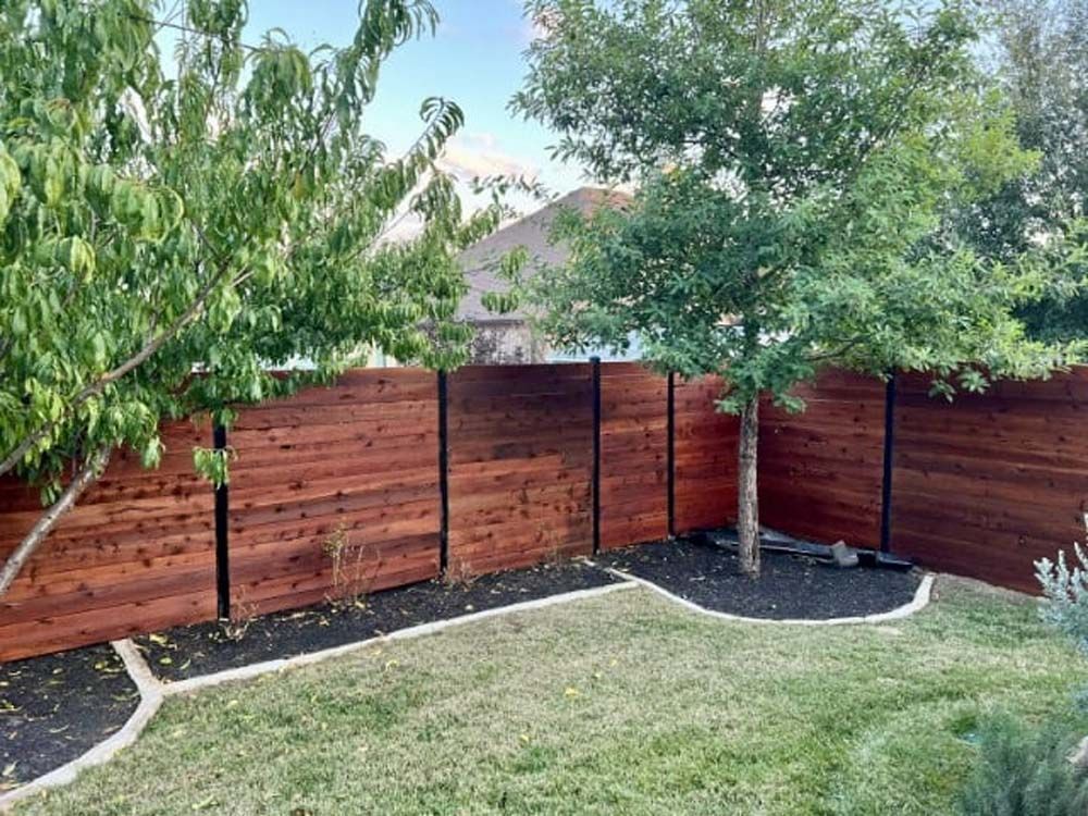 Wooden fence with trees and grass, black mulch border.