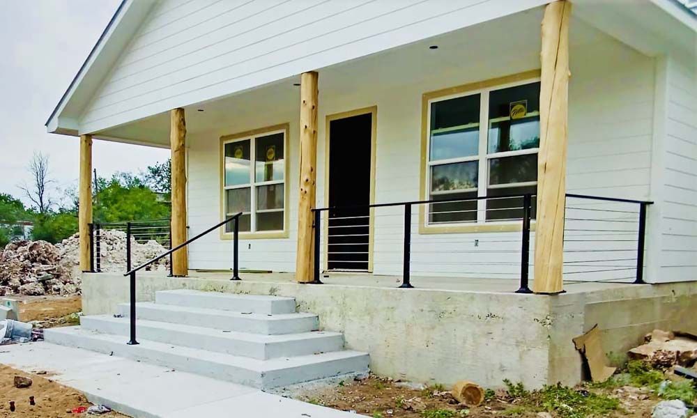 White house under construction with porch, steps, and black railing.