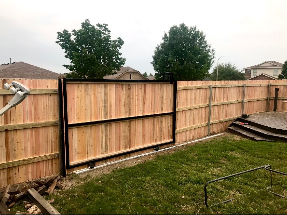 Wooden fence with black gate in a backyard, overcast sky above.