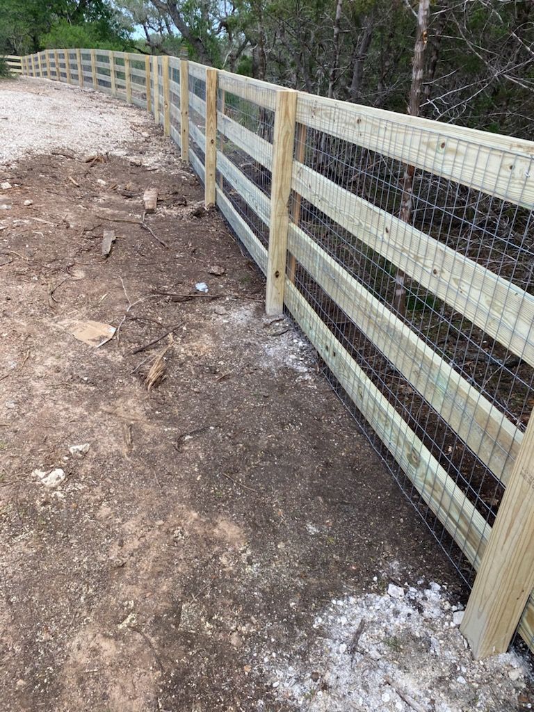 Wooden fence with wire mesh, alongside a dirt path, trees in the background.