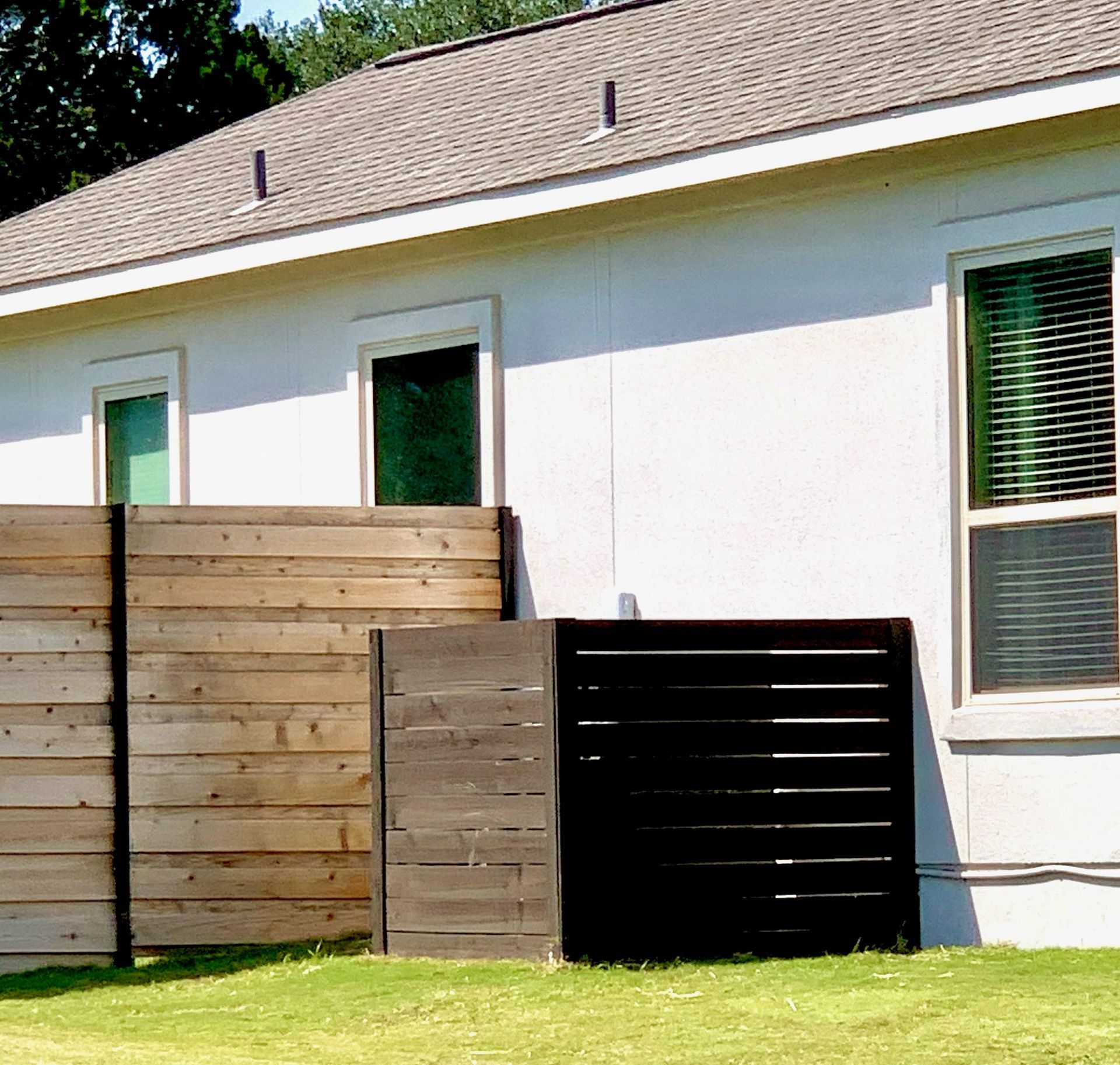 Exterior of a white house with windows and a wooden fence. A black, horizontal-slatted structure is in front.