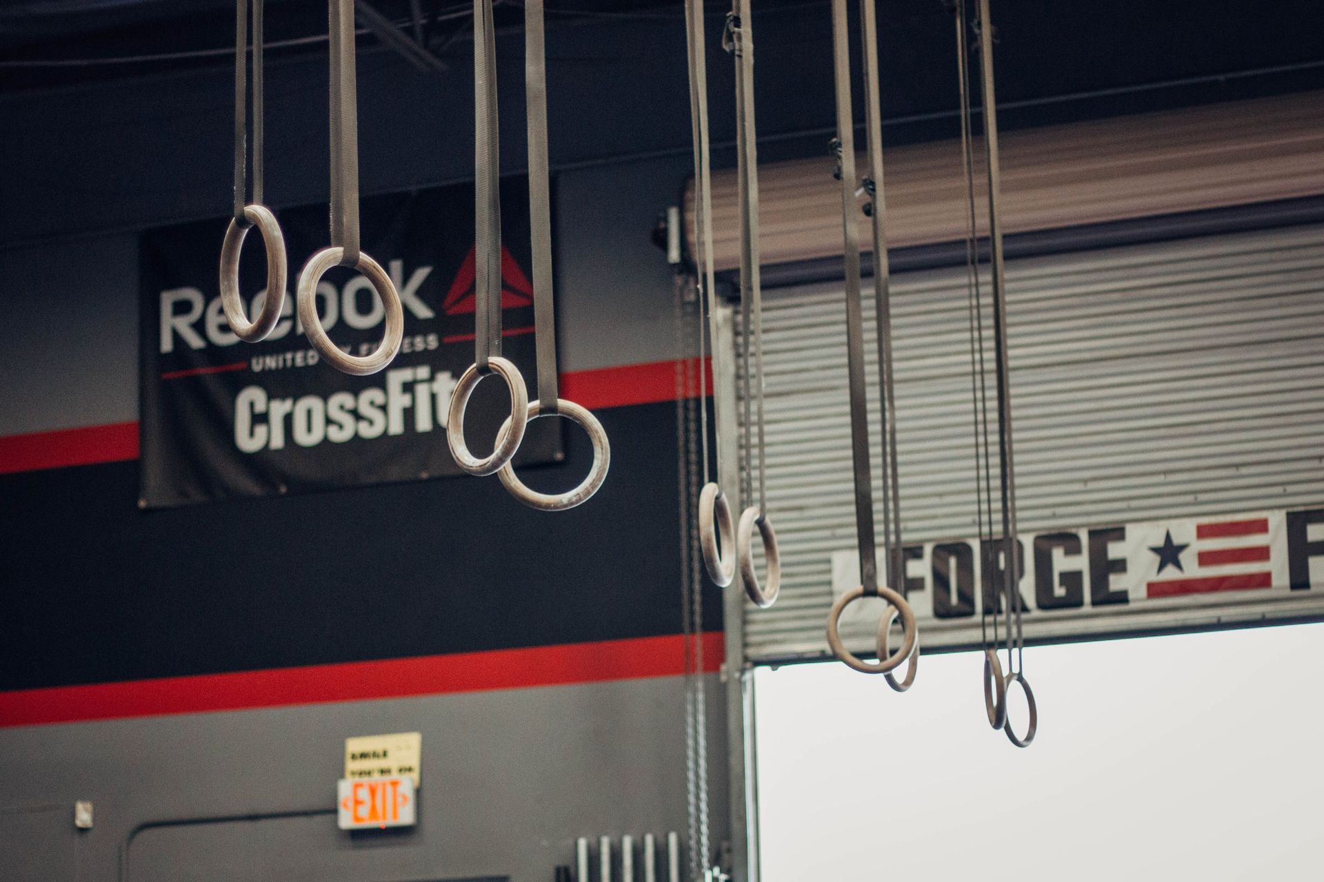 Crossfit rings hanging from the ceiling in front of a sign that says forge