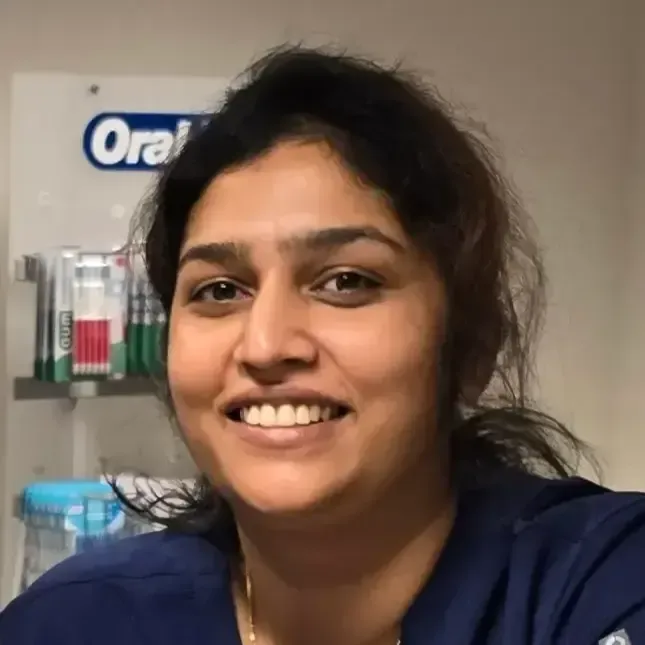 Tannlege Christian med briller og skjegg, iført blå skjorte og medisinsk maske, smiler til kameraet.