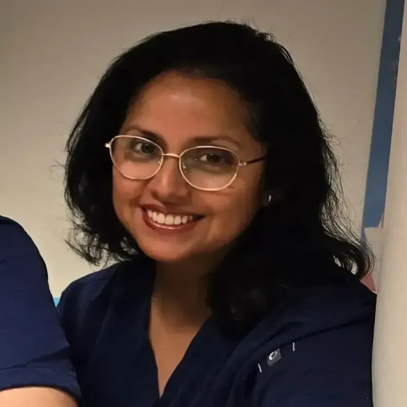 Tannlege Christian med briller og skjegg, iført blå skjorte og medisinsk maske, smiler til kameraet.