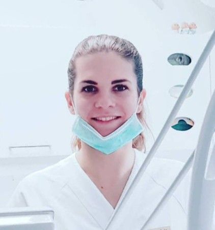 Tannlege Christian med briller og skjegg, iført blå skjorte og medisinsk maske, smiler til kameraet.