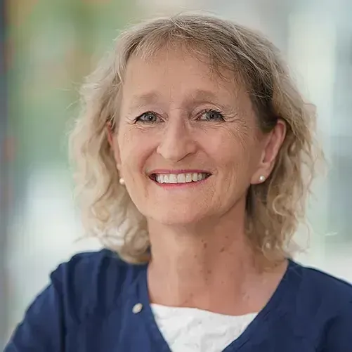 Tannlege Christian med briller og skjegg, iført blå skjorte og medisinsk maske, smiler til kameraet.