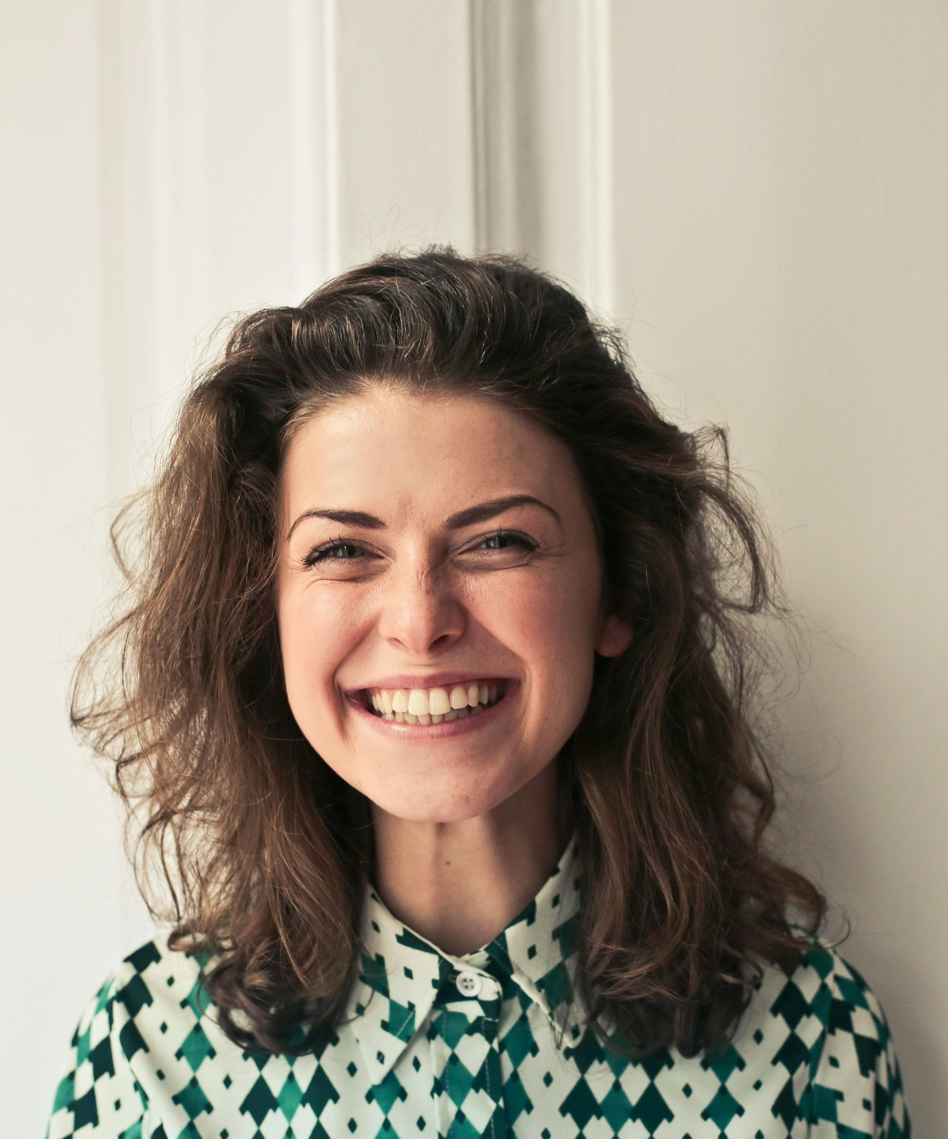 Smilende kvinne, iført en mønstret skjorte, mot en hvit bakgrunn.