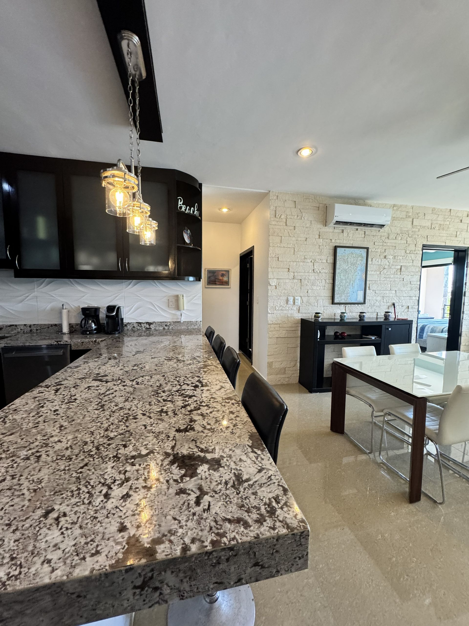 Habitación luminosa con cama gris, decoración de pared tejida, ventilador de techo y puertas corredizas de vidrio que dan al exterior.