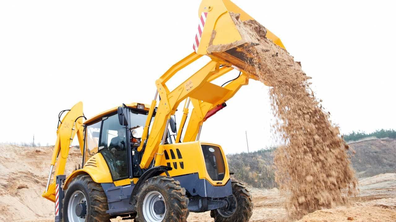 A yellow backhoe excavates dirt from the sand in a construction site.