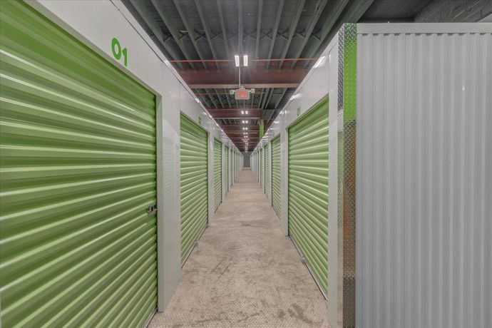 Interior of a storage facility hallway lined with green and white storage unit doors.