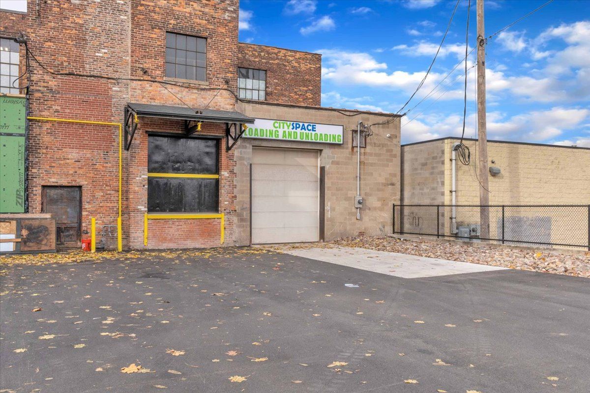 Brick building with a closed garage door and a green sign, with a paved driveway.