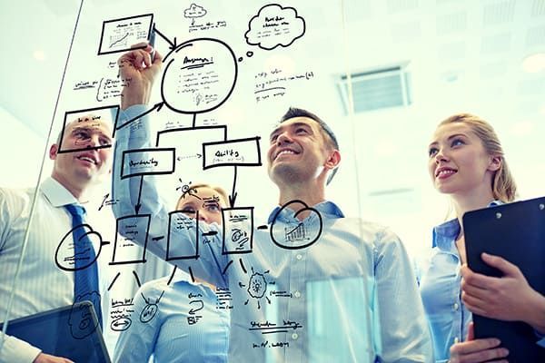 Business team collaborating, drawing diagrams on glass. Smiling, brainstorming ideas in an office.