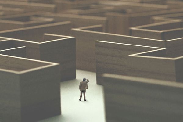 Miniature figure in a wooden maze, looking up, with a questioning expression.