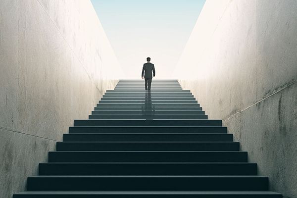 Man in suit walks up a long flight of stairs towards the light.