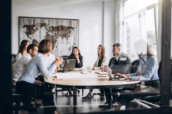 People in business attire at a conference table, discussing ideas. World map art on the wall.