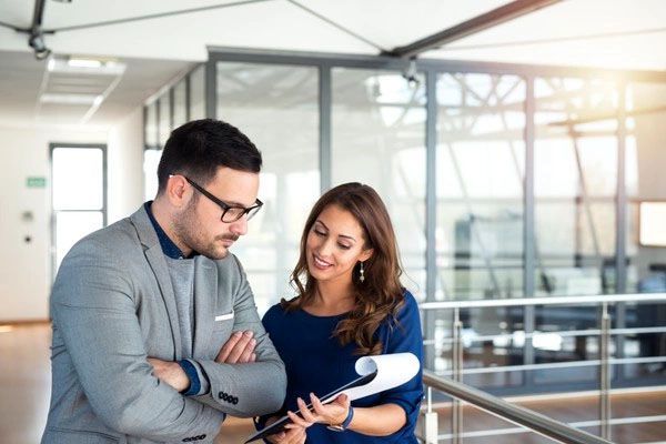 Man in glasses and woman looking at paperwork in a modern office, sunny.