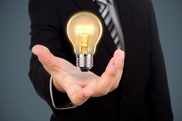 Man in suit holding a glowing lightbulb in his palm, symbolizing an idea.