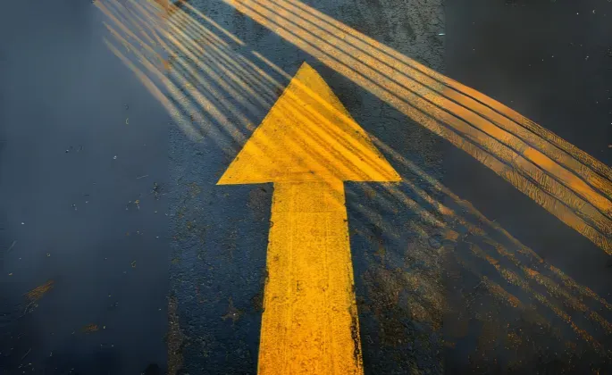 Yellow arrow pointing up on dark pavement, with light streaks.