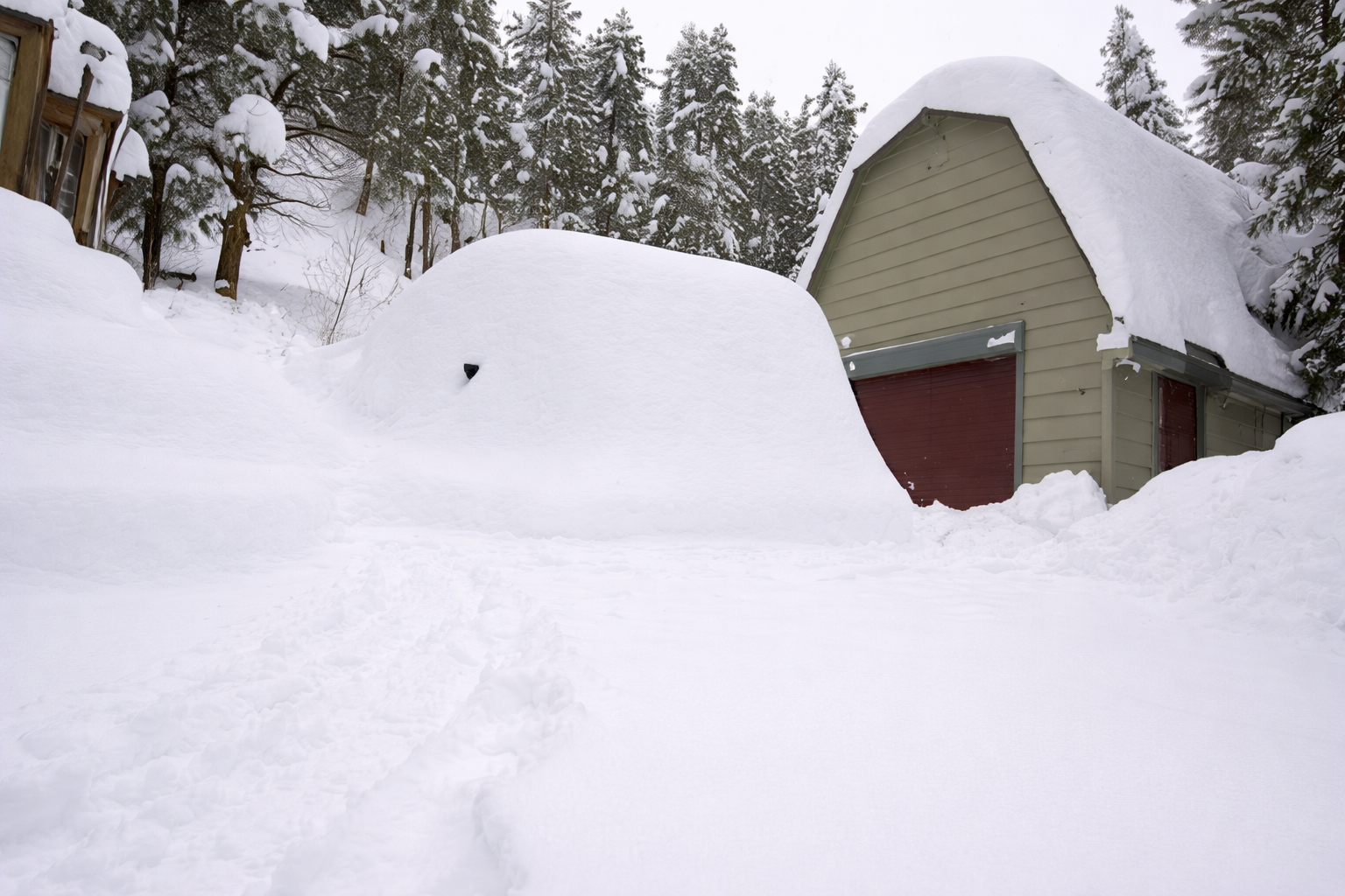 Snow-covered driveway and garage with a huge snowdrift in front of a house.