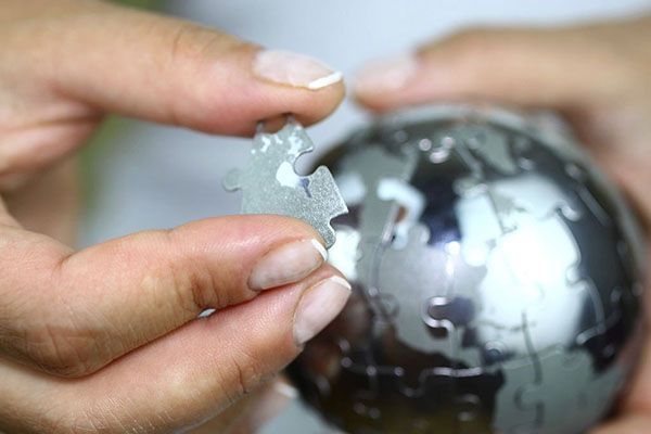 Hands holding a puzzle piece, placing it onto a metallic globe puzzle.
