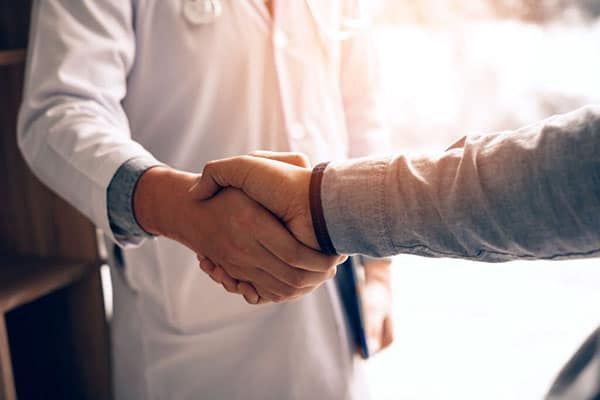 A doctor in a white coat shakes hands with a patient, symbolizing a professional medical agreement or partnership.