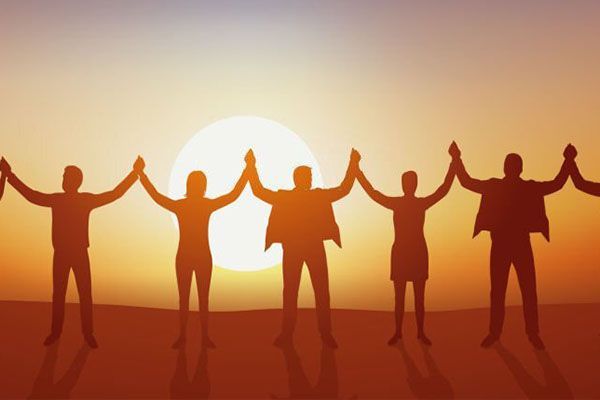 Silhouettes of people standing in a row holding hands against a bright sunrise.
