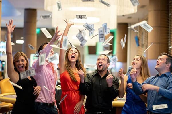 A group of people celebrating in a casino while paper money rains down around them.