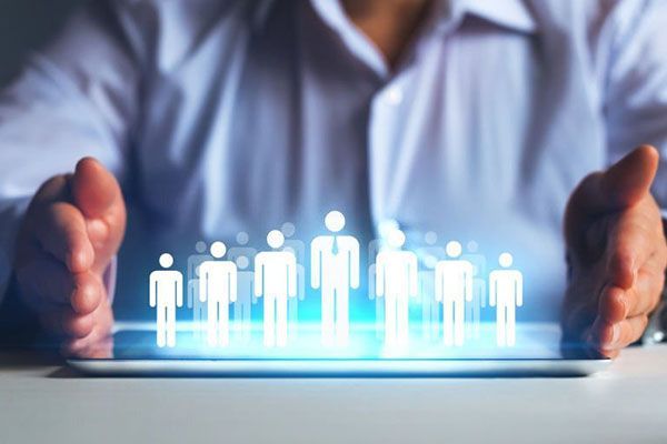 A person in a light blue shirt uses their hands to frame a digital hologram of glowing figures on a tablet screen.