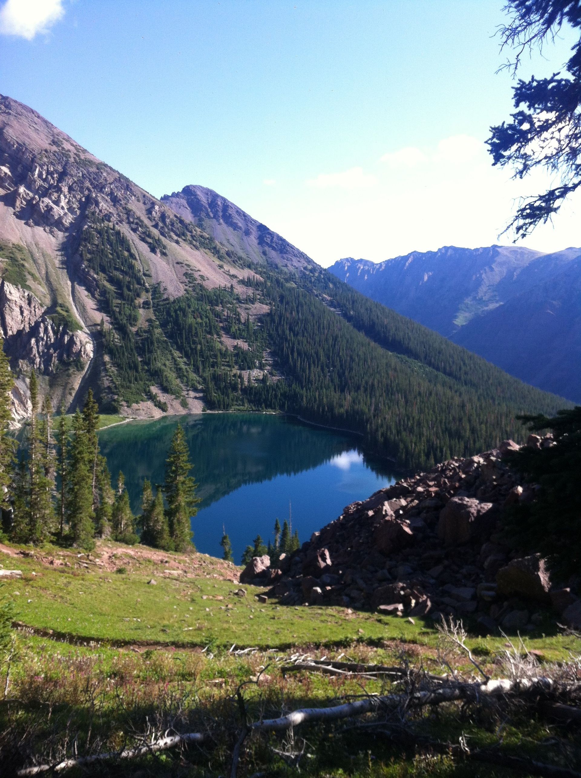 Mountain lake surrounded by forest and mountains, blue water reflects the sky, sunny day.