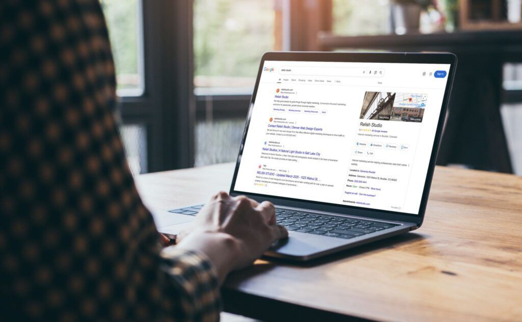 Person using a laptop, likely searching online. Screen displays search results with images and text on a wooden table.