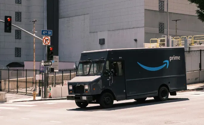 Black Amazon delivery truck at a city intersection, driving past a traffic light.