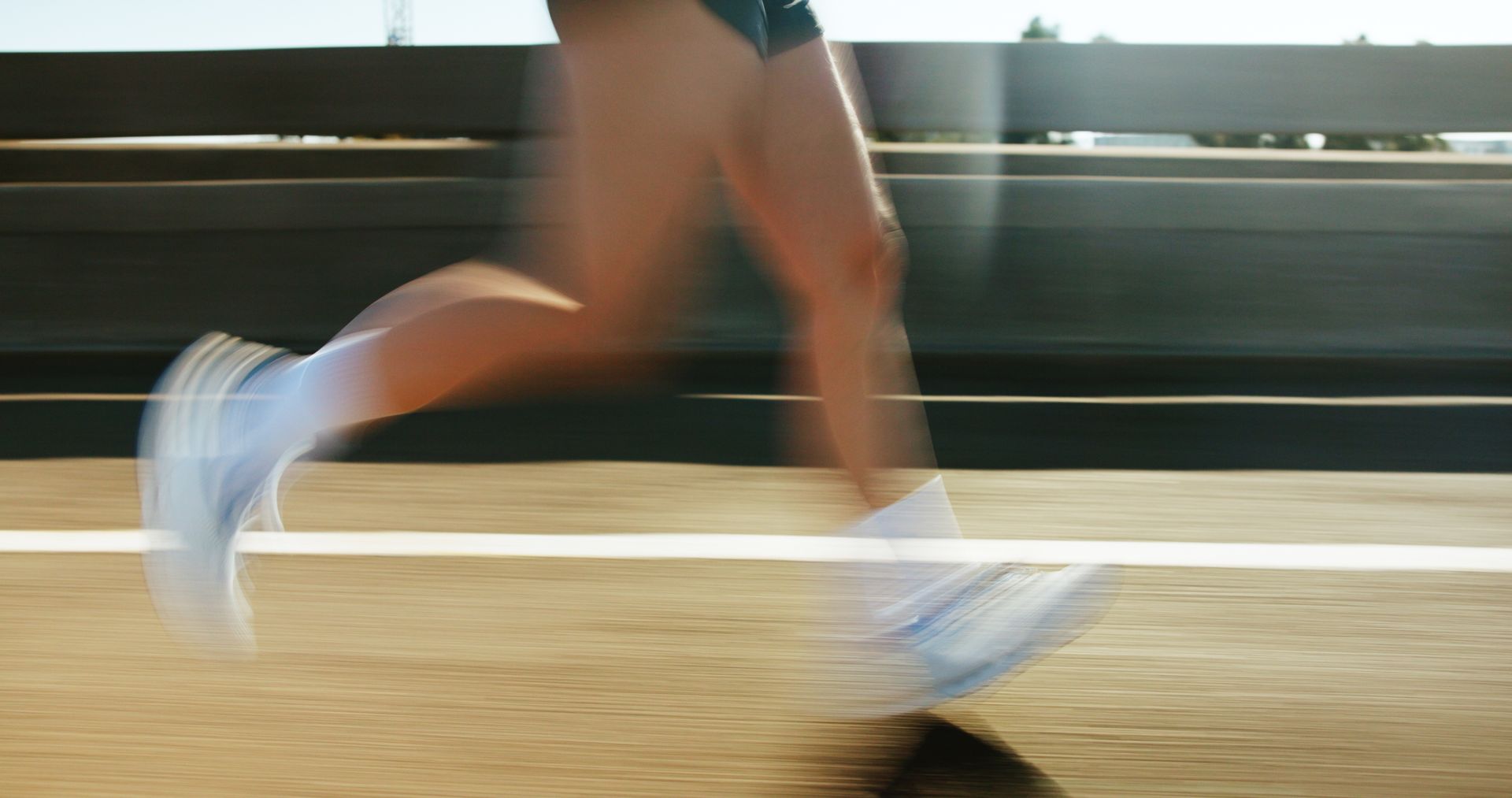 A runner's legs and feet in white shoes speeding along a track, blurred motion.