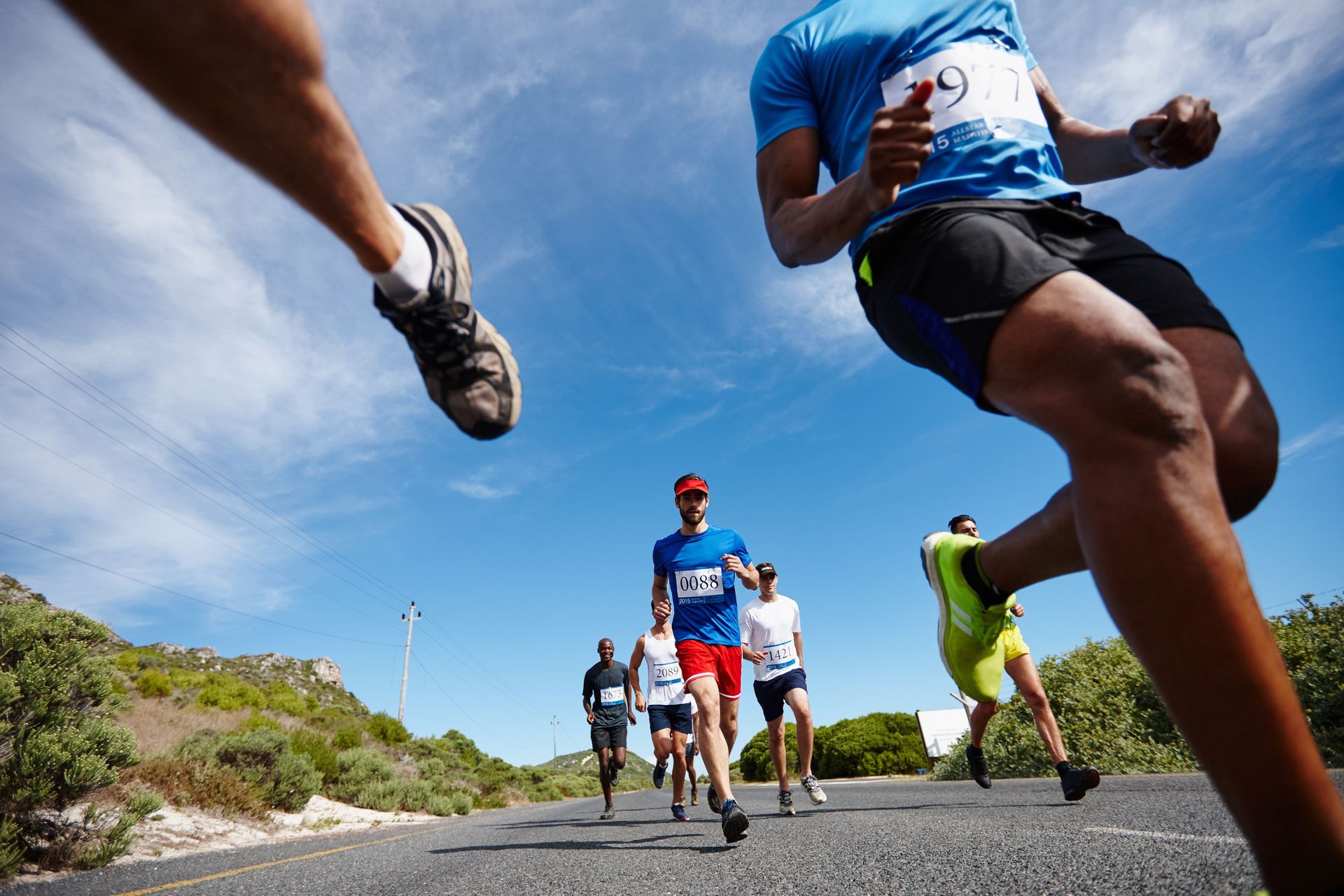A low-angle view of a group of runners competing in an outdoor race on a paved road under a clear blue sky.