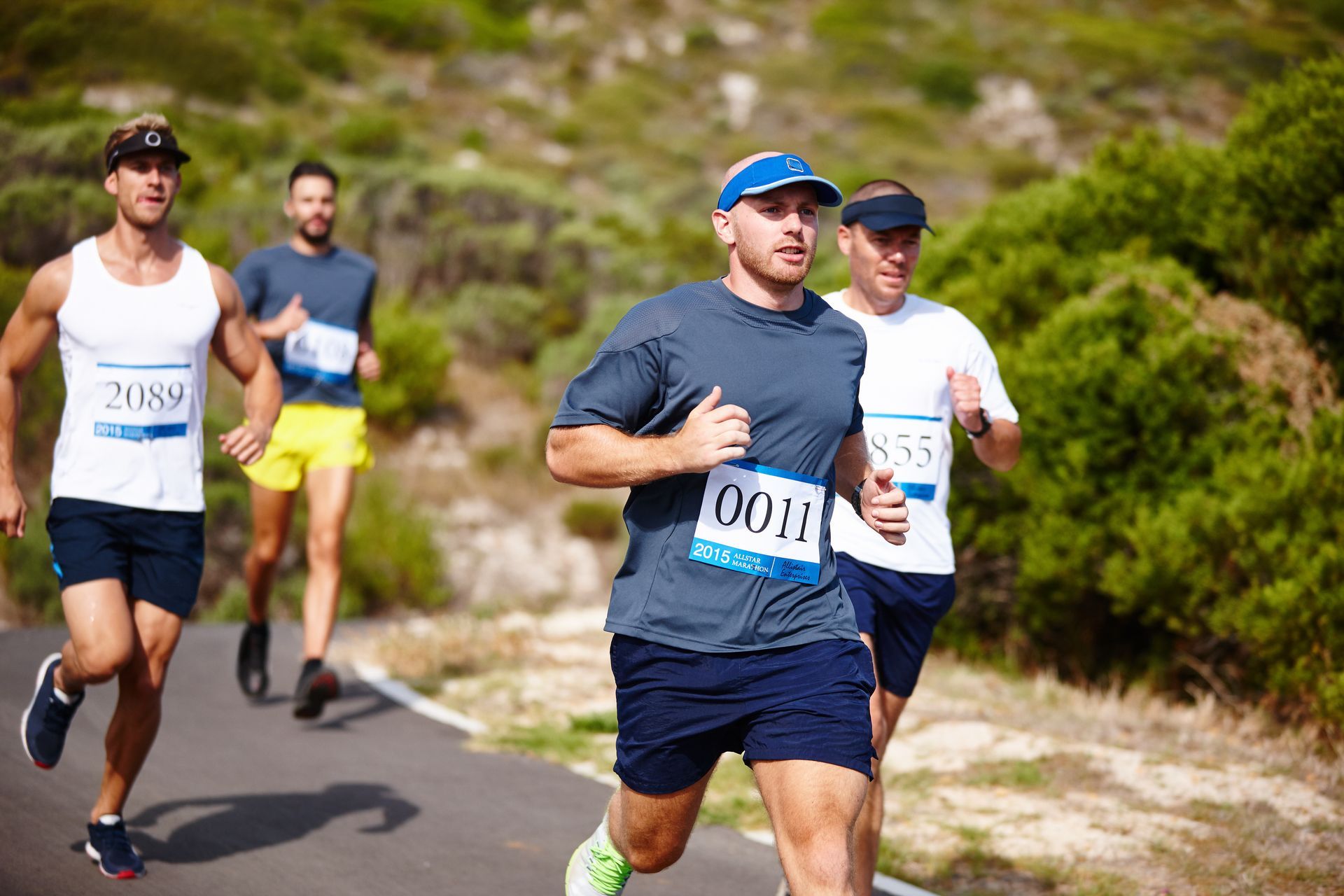 Four runners in athletic wear and race bibs jog along an outdoor paved path during a race.