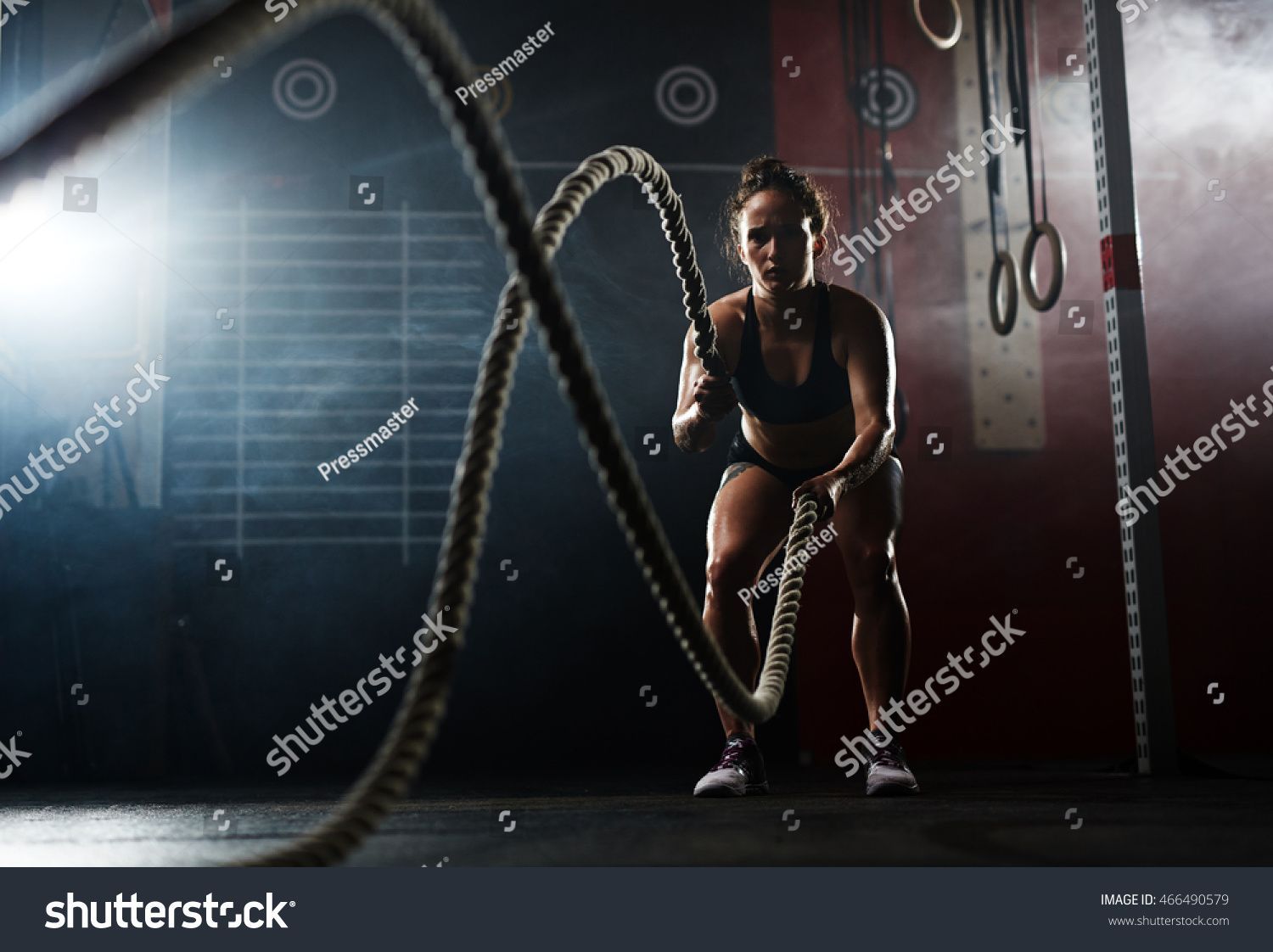 Woman exercising with battle ropes in a gym, smoky background.