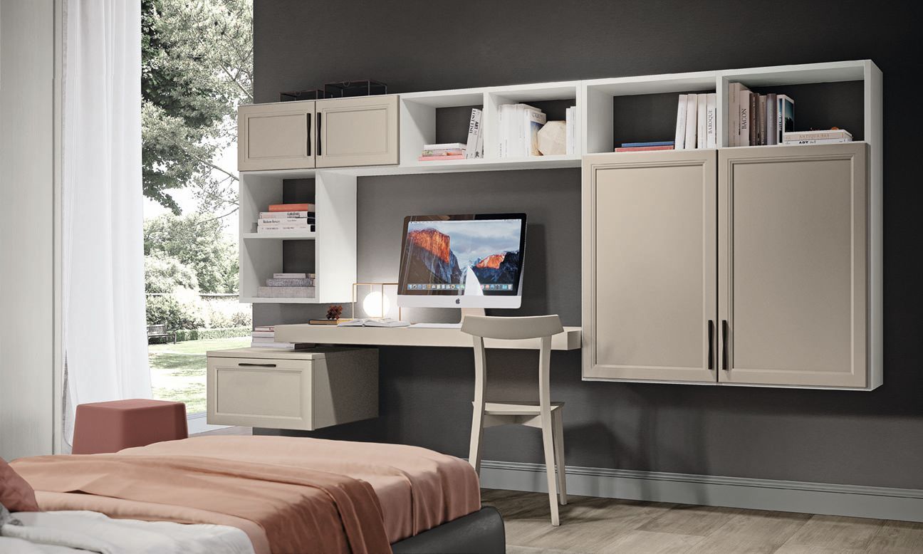 Camera da letto con scrivania, computer e scaffali integrati; mobili beige e bianchi contro una parete grigia.