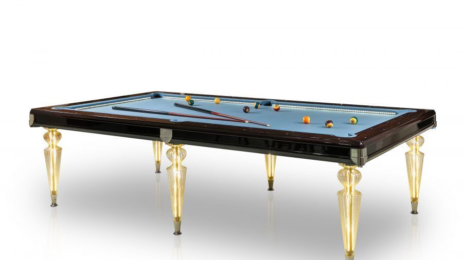 Tavolo da biliardo con feltro azzurro, finiture in legno scuro e gambe decorative color oro, con palle da biliardo e stecche.