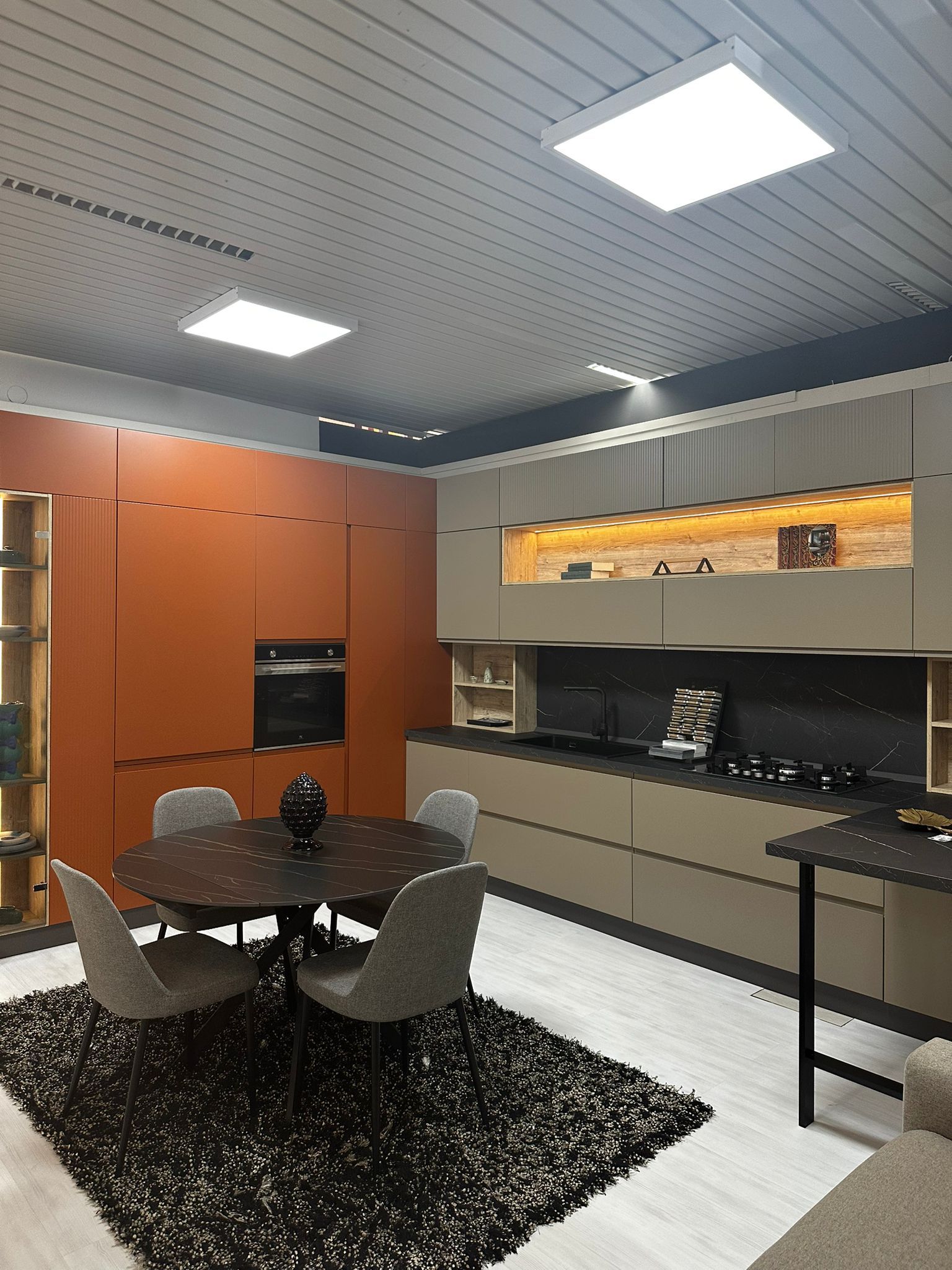 Cucina moderna con mobili arancioni e beige, tavolo rotondo con sedie e tappeto nero.